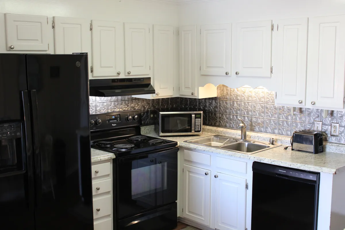 A functional and welcoming kitchen space equipped with black appliances, granite countertops, and a decorative backsplash. The setup is designed for cooking and family gatherings, and hints at the versatility for everything from baking sessions to dinner parties.