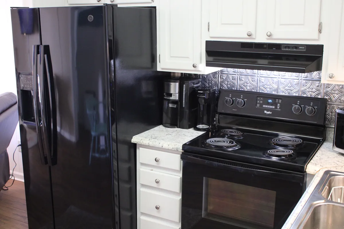 A modern kitchen featuring a black refrigerator and stove, granite countertops, and white cabinetry. The layout is open and inviting, with plenty of counter space for meal prep or gathering together. The scene subtly suggests the potential for family or group cooking sessions, highlighted by clean lines and contemporary style.