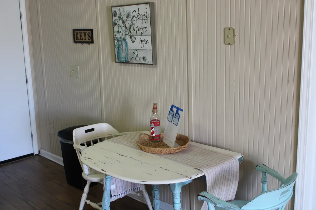 A cozy dining nook with a small round table and blue-green chairs, accented by decorative wall art. The setup encourages intimate meals or morning coffee, fostering a warm and sociable vibe.